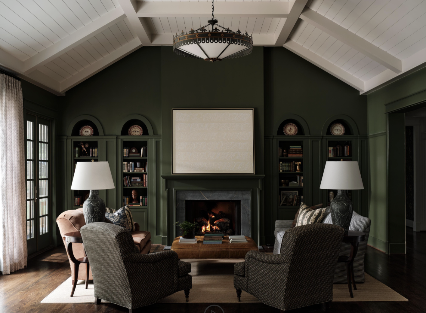 There was a time when open floor plans felt like the ultimate luxury. But lately, we have noticed a shift to rooms with a purpose. Love a library with Visual Comfort brass library lights and beautiful moody blue walls - Sabbe Interior design | Joseph Bradshaw Photography - Beautiful living room in moody green with paneled ceiling