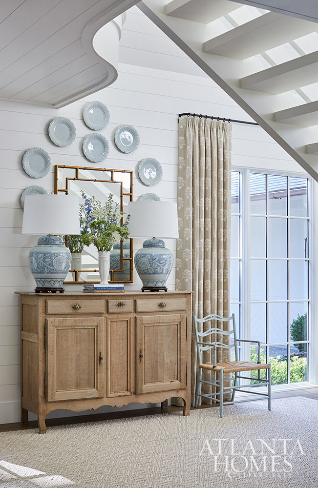 The era of the mountain home of yesterday is over, and today's modern mountain retreat is warm, effortless, and quietly elegant. white paneled walls in the entrance foyer with blue plate surrounding a mirror over a wood chest with blue and white lamps SOURCE; Atlanta Homes & Lifestyles INTERIOR DESIGN  Virginia Nocharli Design  ARCHITECT: Greg Busch Architects BUILDER Rhett Bonner, Bonner Buchanan  LANDSCAPE ARCHITECT  Richard Anderson Landscape Architect