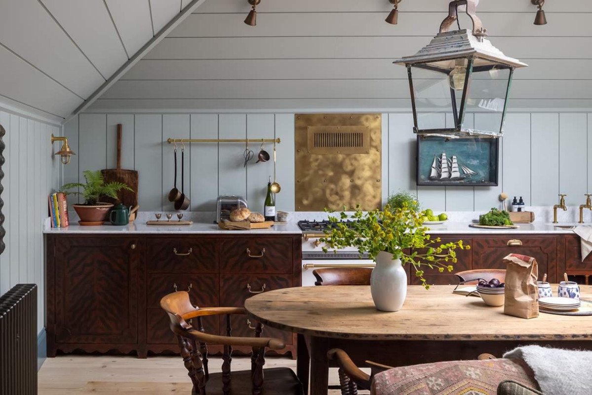 This former fisherman's house, imagined as a sea captain's home, is totally unique, quietly luxurious, and unforgettably chic. Ham Interiors - Alexander James Photography - charming kitchen and dining room combination with shiplap walls and lantern over the dining table - love the hanging brass rack