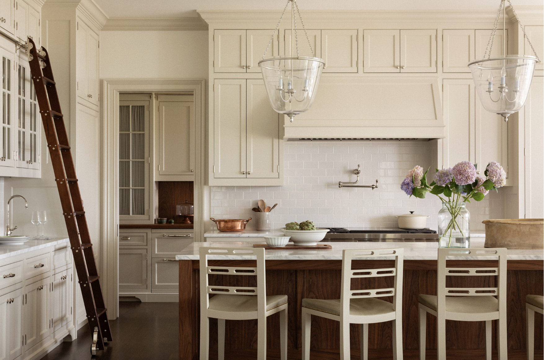 Beauty, sophistication, and attention to detail are just a few of the things that come to mind when we think of Marianne Simon Interiors' beautiful designs. It’s those little things that we think make Simon’s work shine the very most.Neutral kitchen with bell jar lights over isalnd