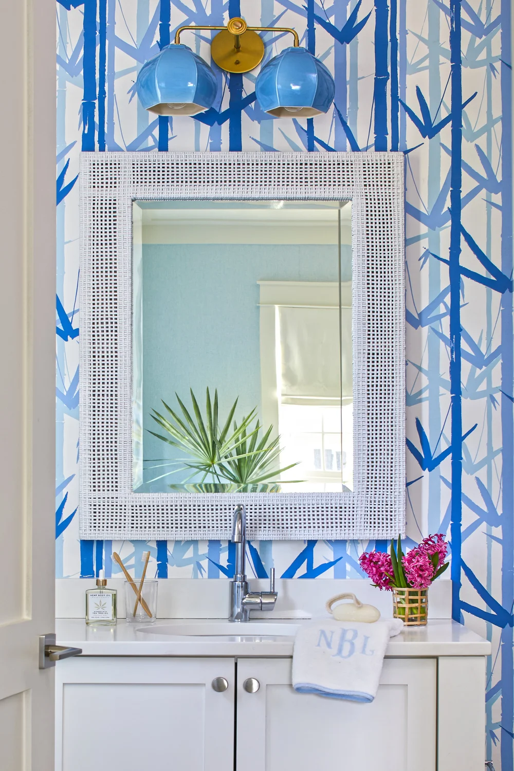 Sometimes a blue and white palette can feel predictable, but in this utterly charming Kara Miller-designed beach house, photographed by , Laurey W. Glenn and styled by Lindsey Ellis Beatty, it feels fresh and inviting. The various color tones, natural materials, and textured accents ground each space, creating a livable home with plenty of style. Blue and white beach house bathroom with charming palm leaf wallpaper