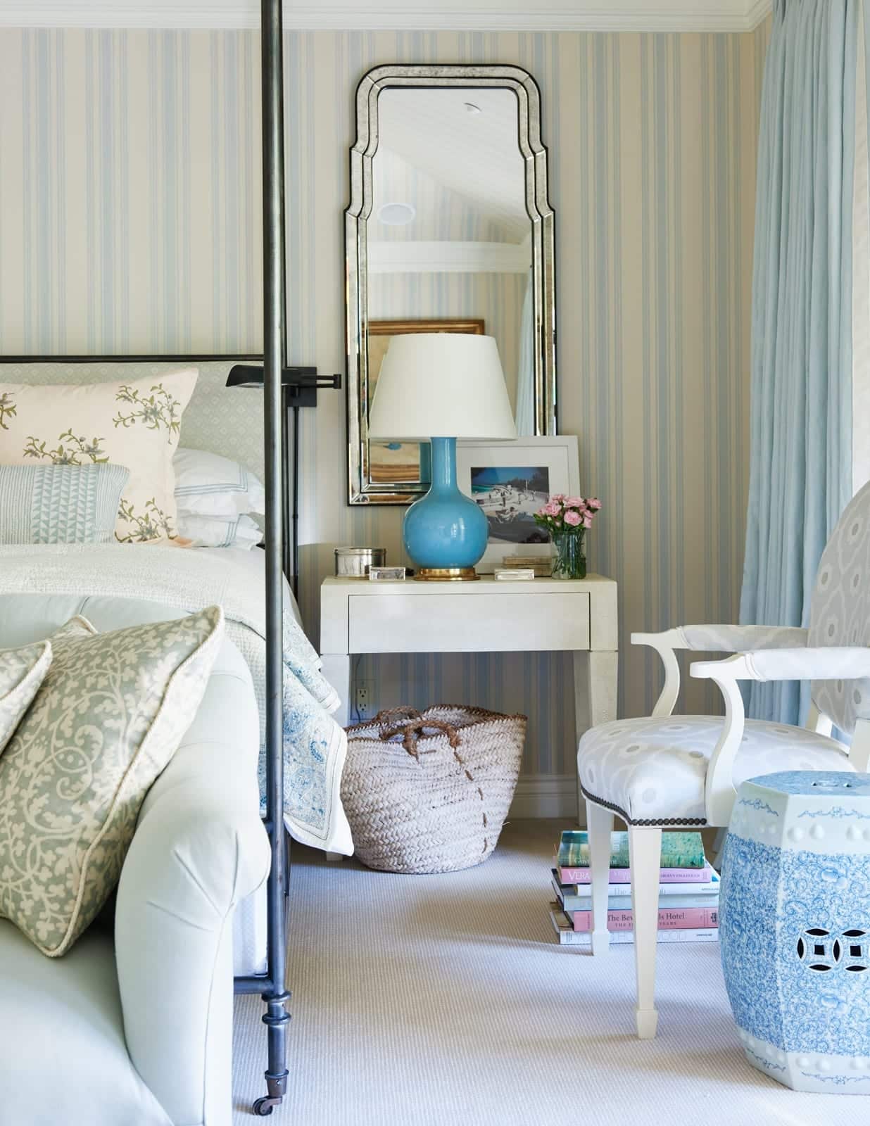 Blue and white bedroom with blue and white striped wallpaper and a black iron four-poster bed with classic furnishings and layered decorative accents