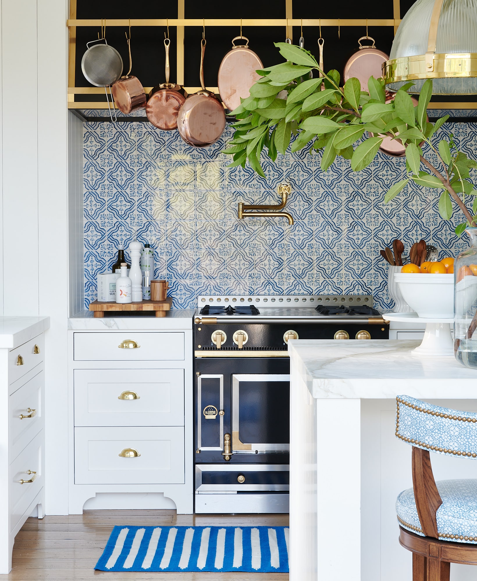 Blue and white tile backsplash in a white kitchen with hanging copper pots