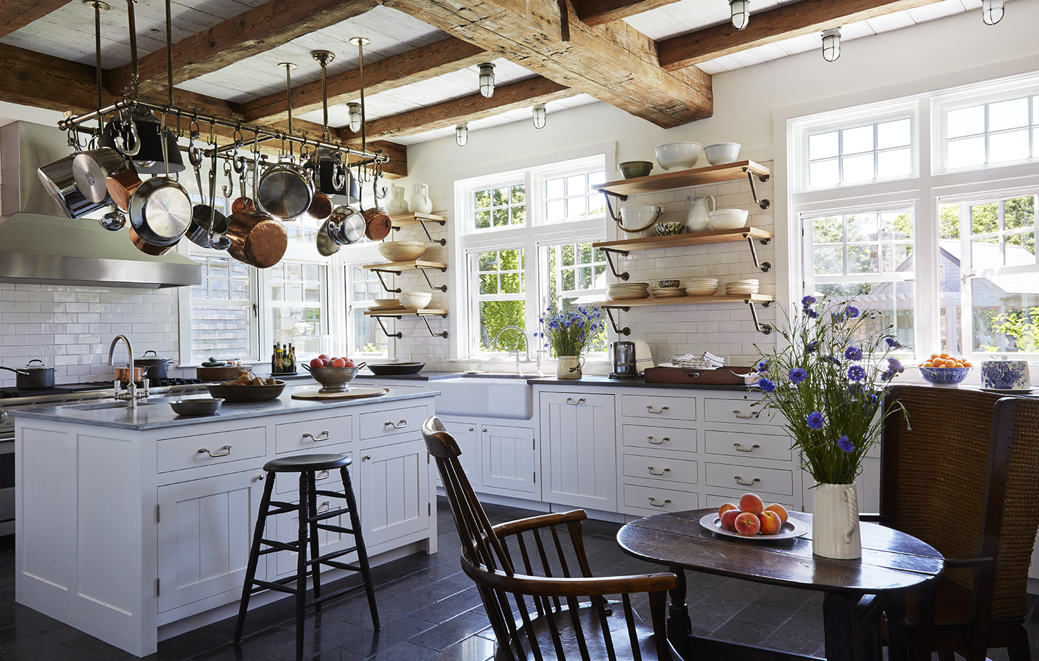 Classic white kitchen showcasing a collected home look with hanging copper pots, wood beams, and timeless traditional design