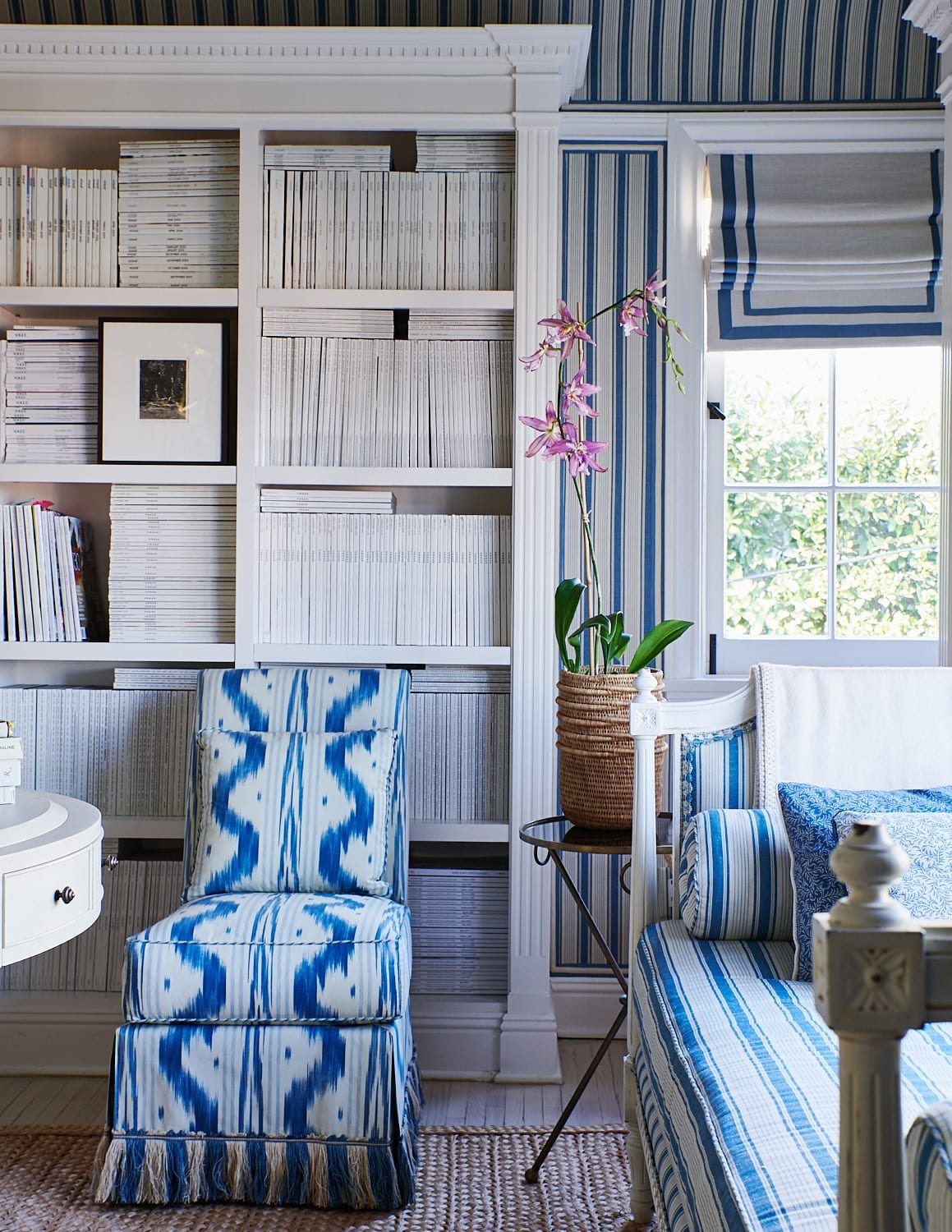 Classic living room with blue and white striped daybed and chair with a bookcase filled with magazines