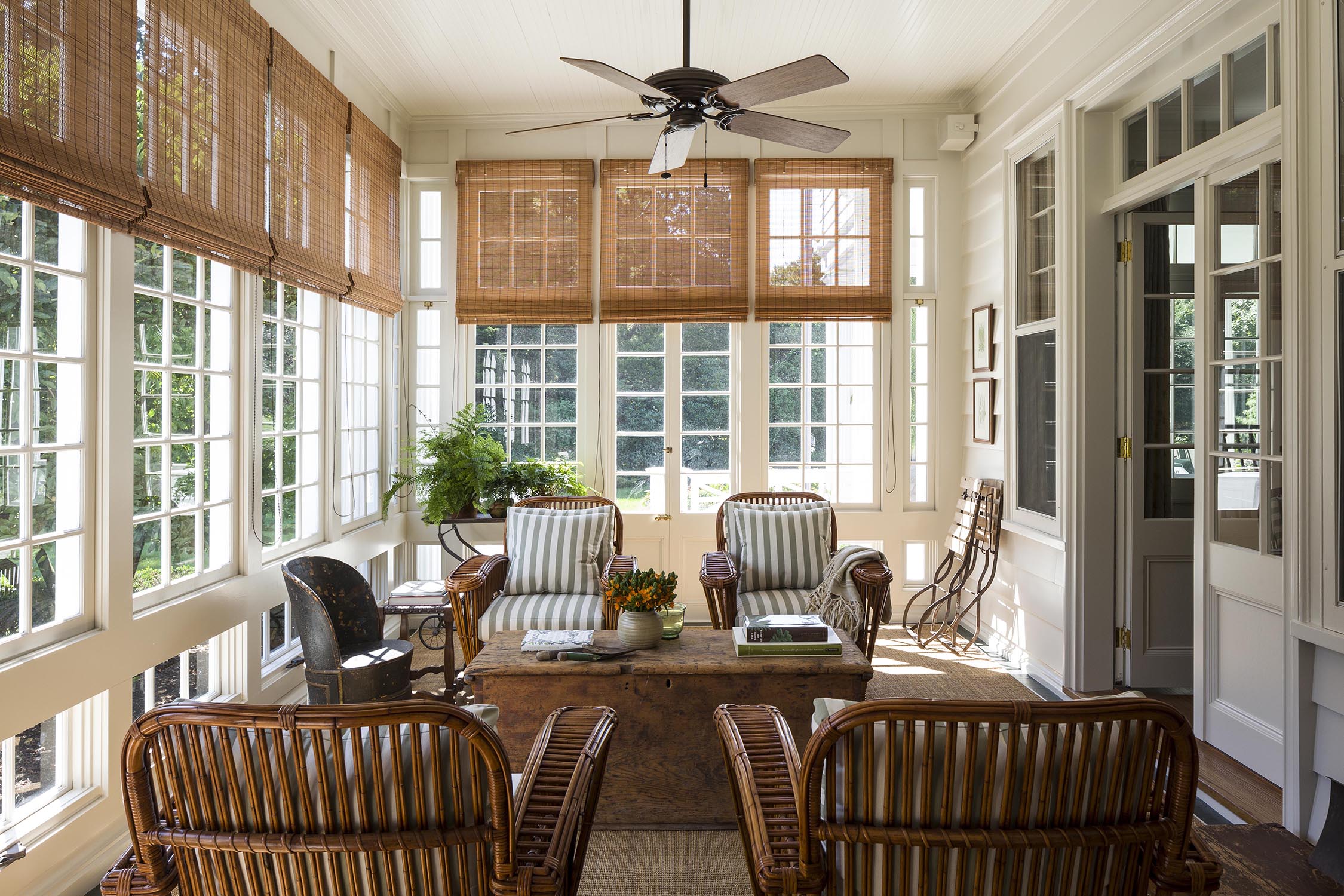 Charming porch with wicker furniture, large windows, bamboo shades, and a traditional collected home look