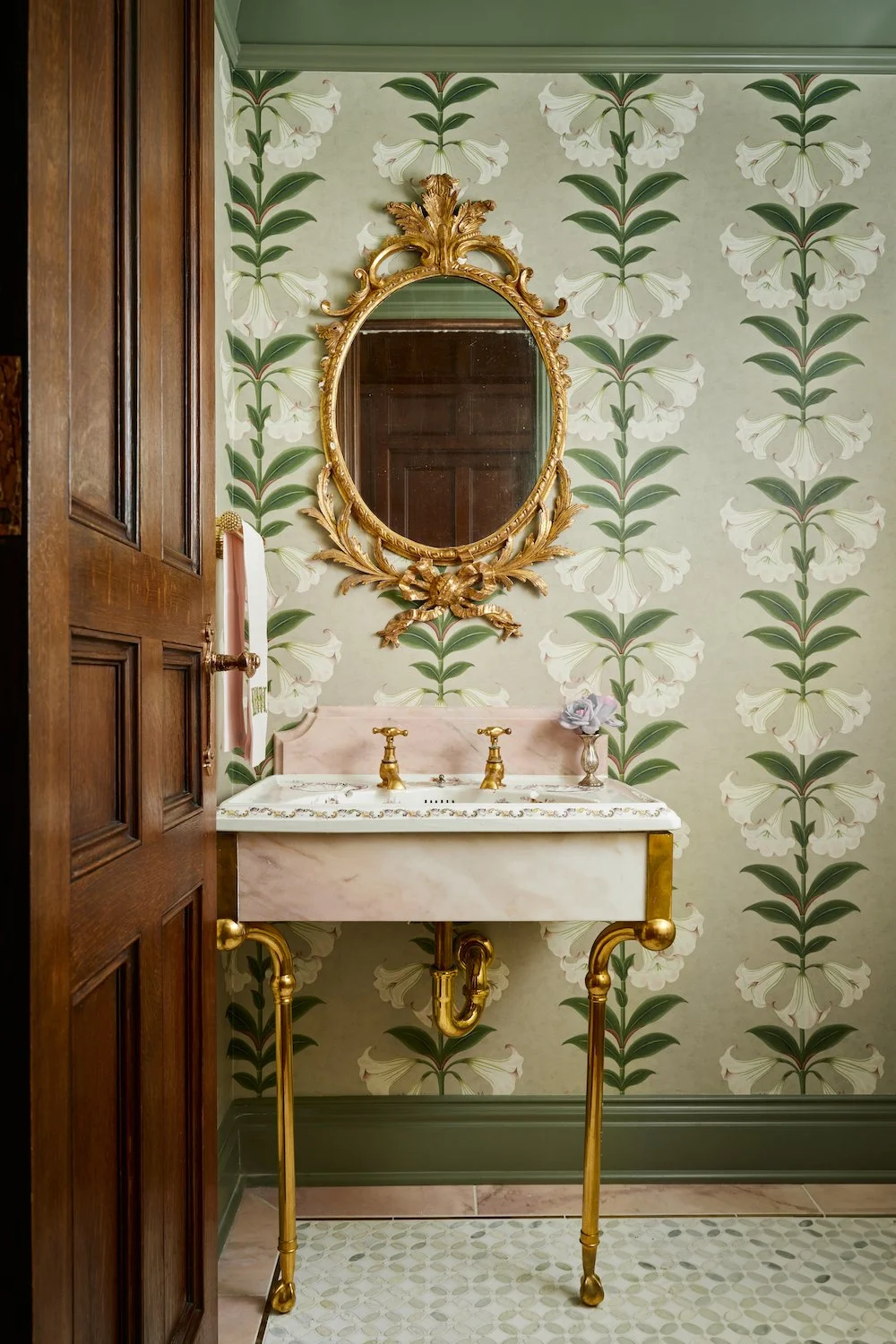 Soft and romantic powder room showcasing Cole and Son Angel’s Trumpet wallpaper over a custom soft pink bathroom vanity cabinetry.