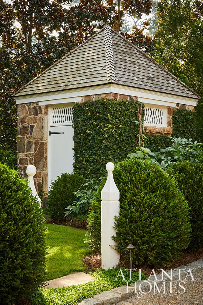 Stone outbuilding in this Dutch Colonial home with ivy growing and boxwoods