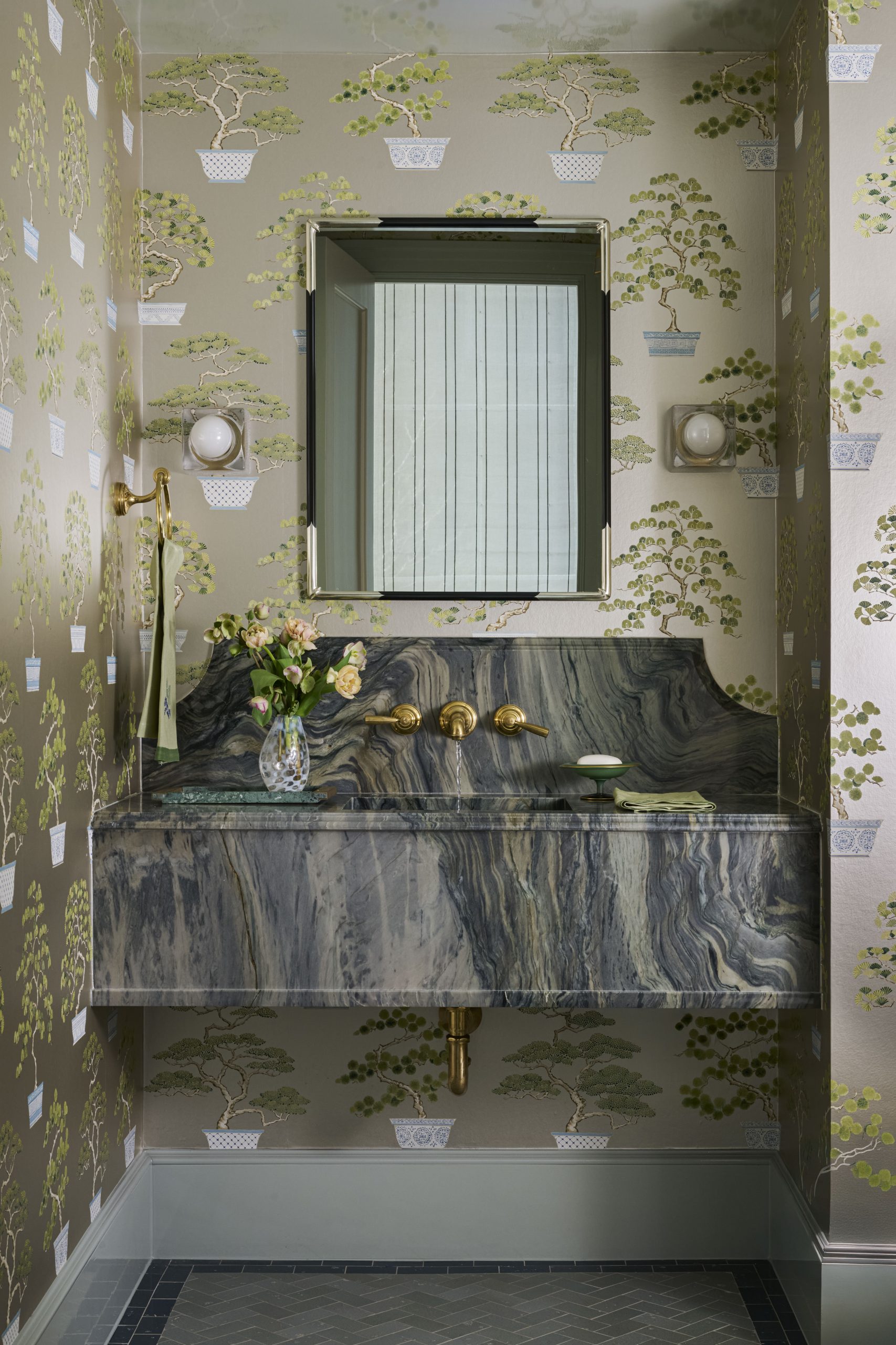 Grandmillennial style powder room clad in dark green Sanderson Penjing botanical wallpaper with a rustic hanging stone basin sink.