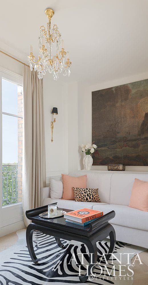Paris is always a good idea, and when Ann Huff of Huff Harrington is designing your Paris apartment, it's an even better one! White sofa in the living room with leopard pillows and a large crystal chandelier and black coffee table - Source: Atlanta Homes & Lifestyles | Interior Design: Ann Huff, Huff Harrington |  Photographed by Joan Porcel