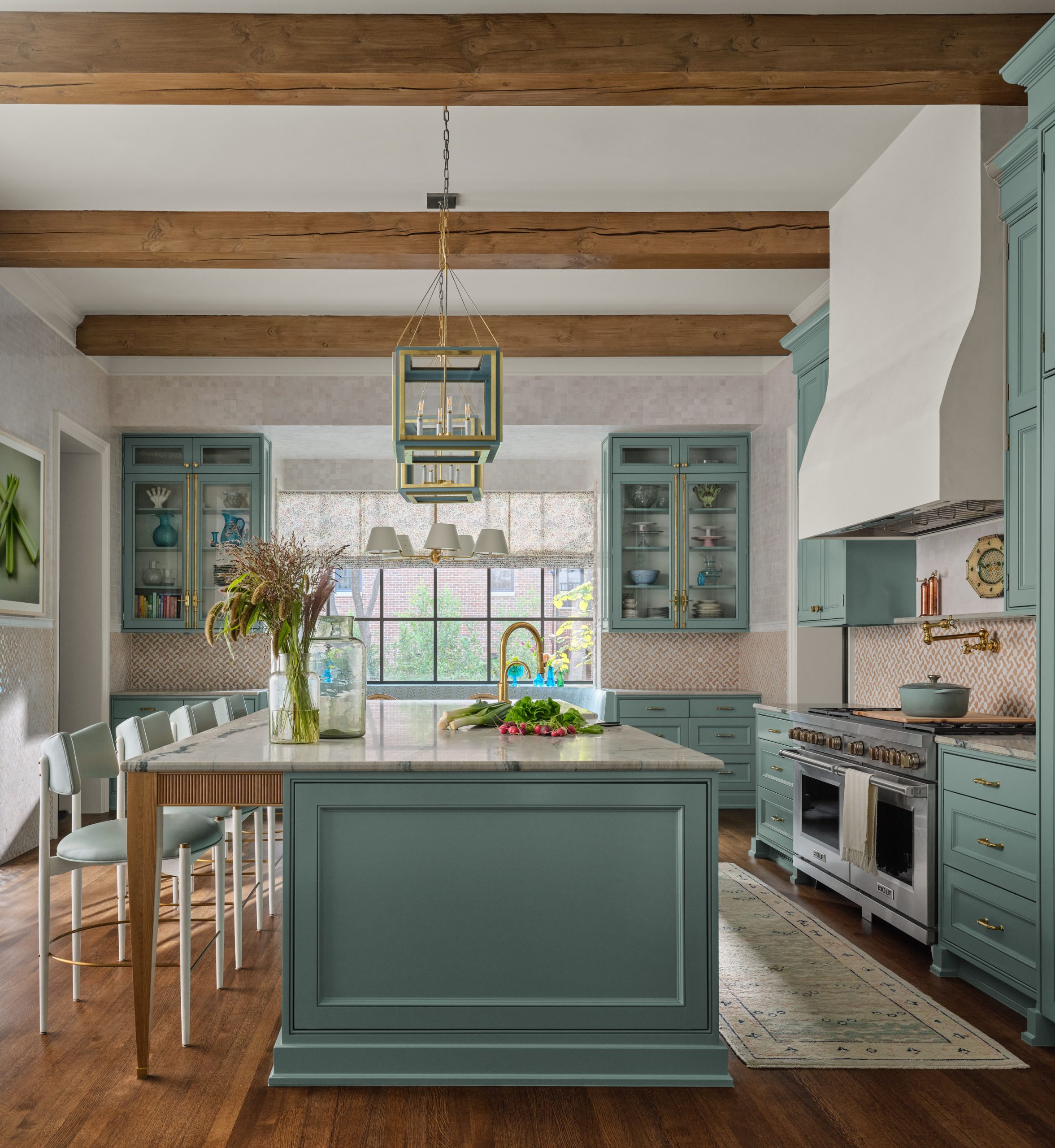 Luxury kitchen featuring light blue cabinets, a matching blue center island with a marble countertop, wood ceiling beams, a double-oven range with a white hood, and modern bar stools designed by Collins Interiors.