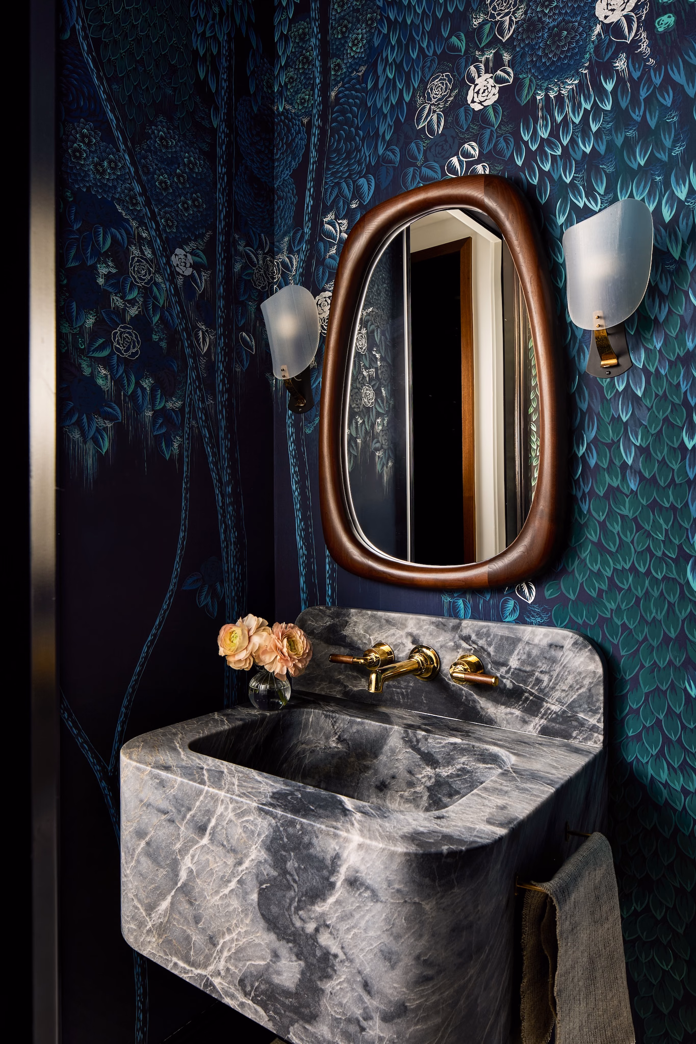 High-contrast maximalist powder room with a custom-carved floating stone sink set against deep inky blue Hippolyta de Gournay scenic wallpaper.