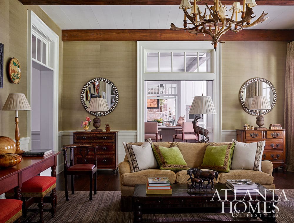 Living room with gold velvet sofa, a pair of antique chests with round mirrors over them and an antler chandelier